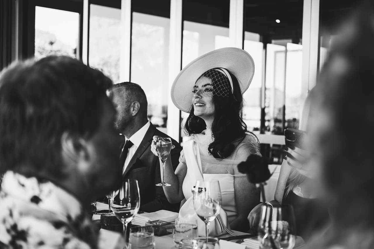 Black and white photo of Kim laughing at the dinner table with a glass in her hand, Ben beside her