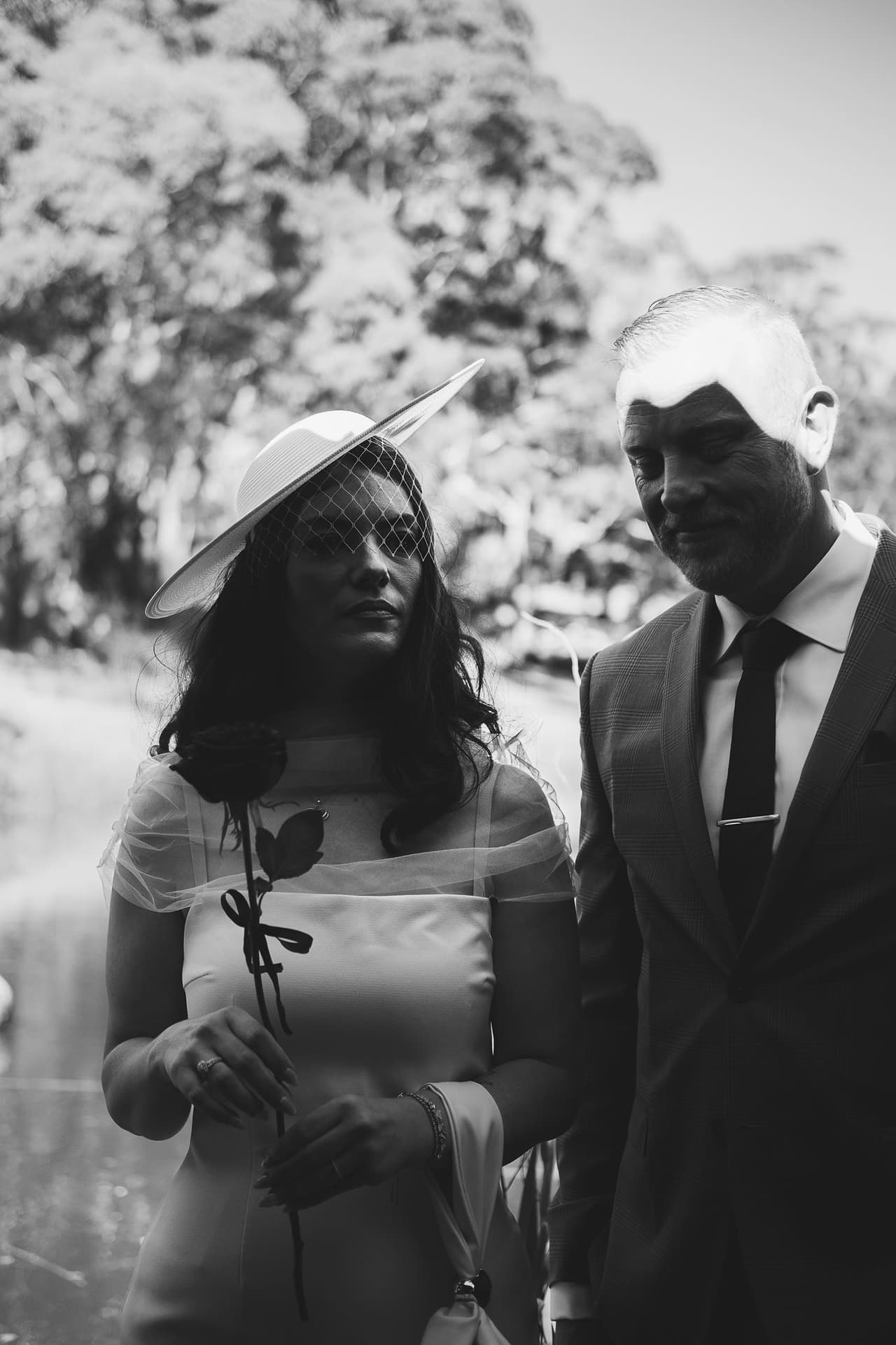 Black and white photo of Kim in her wide-brimmed hat holding a single rose, Ben beside her