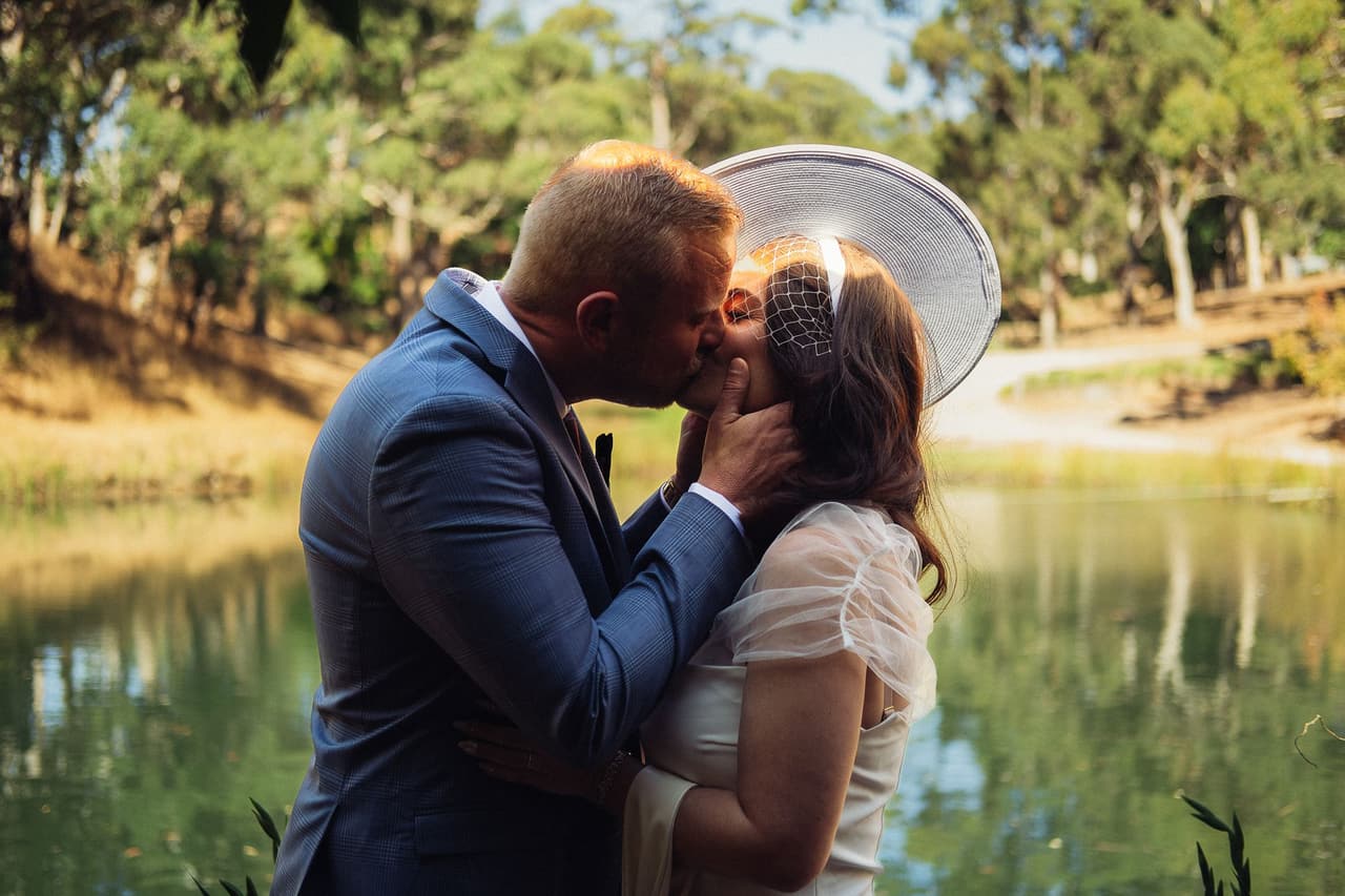 Ben holding Kim’s face as they kiss at the end of the ceremony, the pond behind them