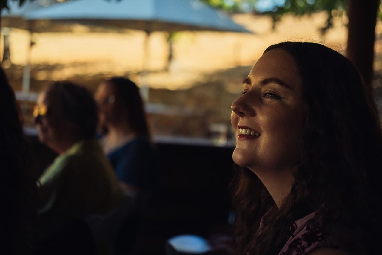 A guest smiling as she watches the ceremony from the shade of the Boatshed