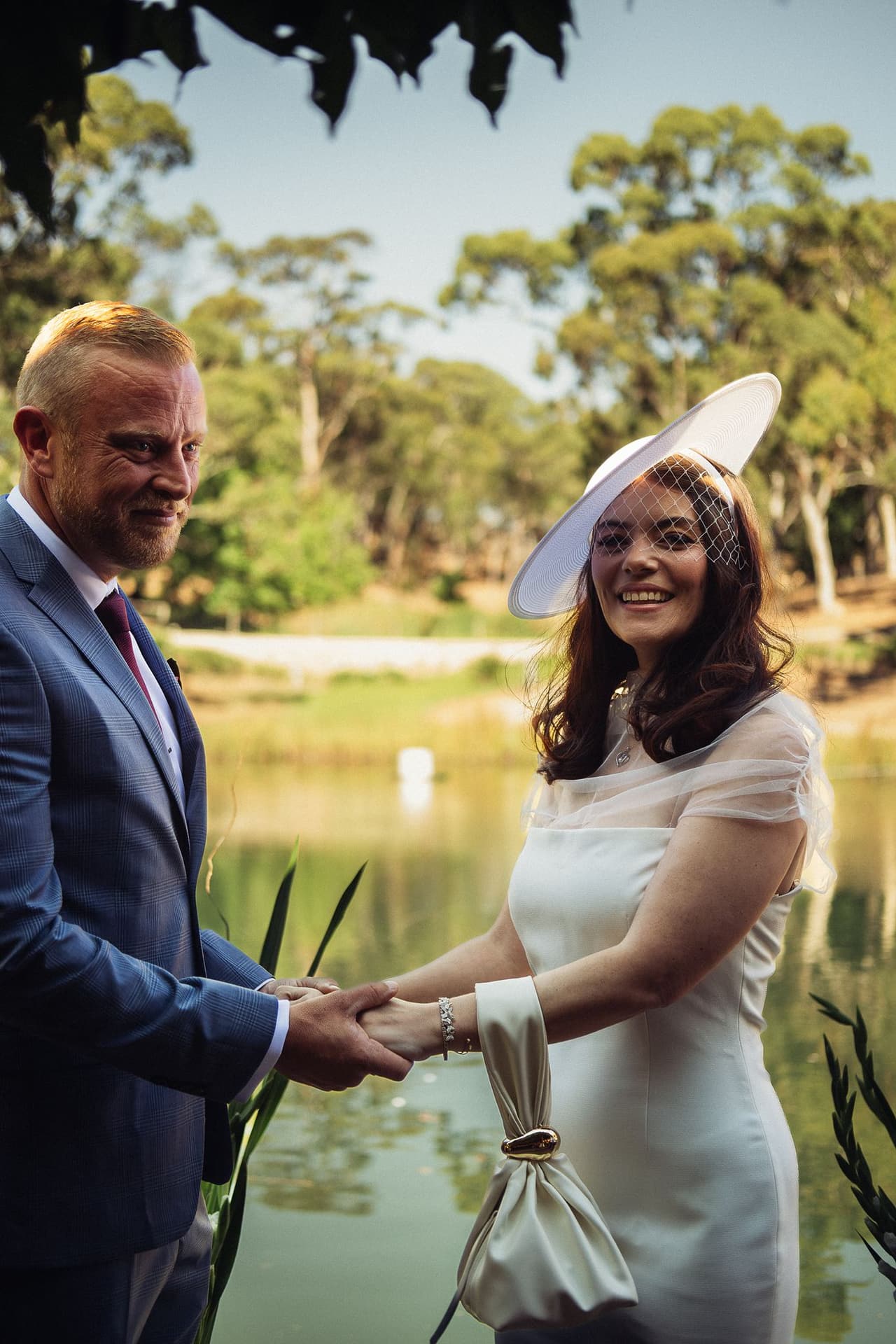 Kim beaming as she holds Ben’s hands on the deck, the pond and gum trees behind them