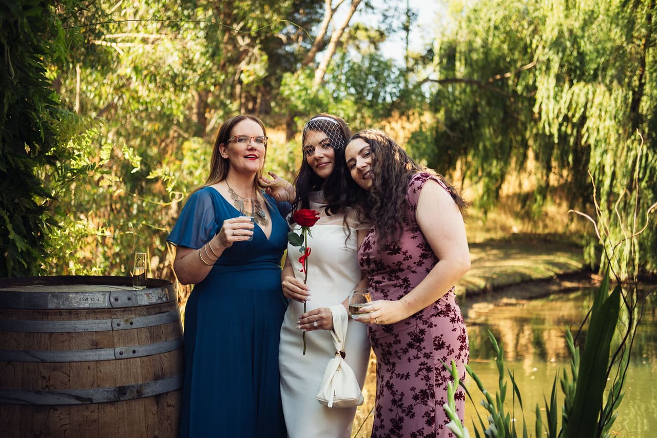 Kim between two women by the wine barrel on the deck, one resting her head on Kim’s shoulder