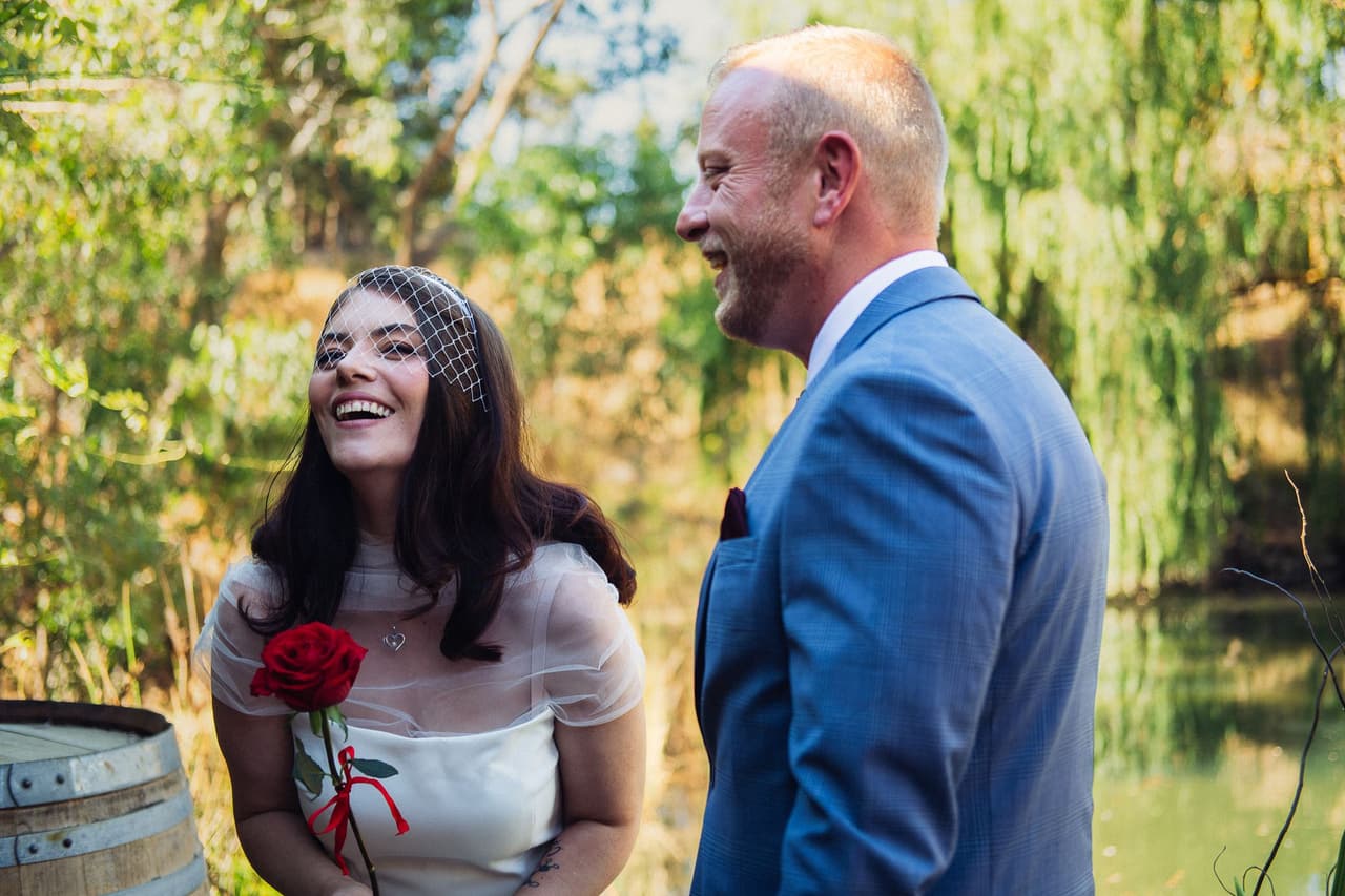 Kim laughing up at Ben by the wine barrel, a red rose in her hand