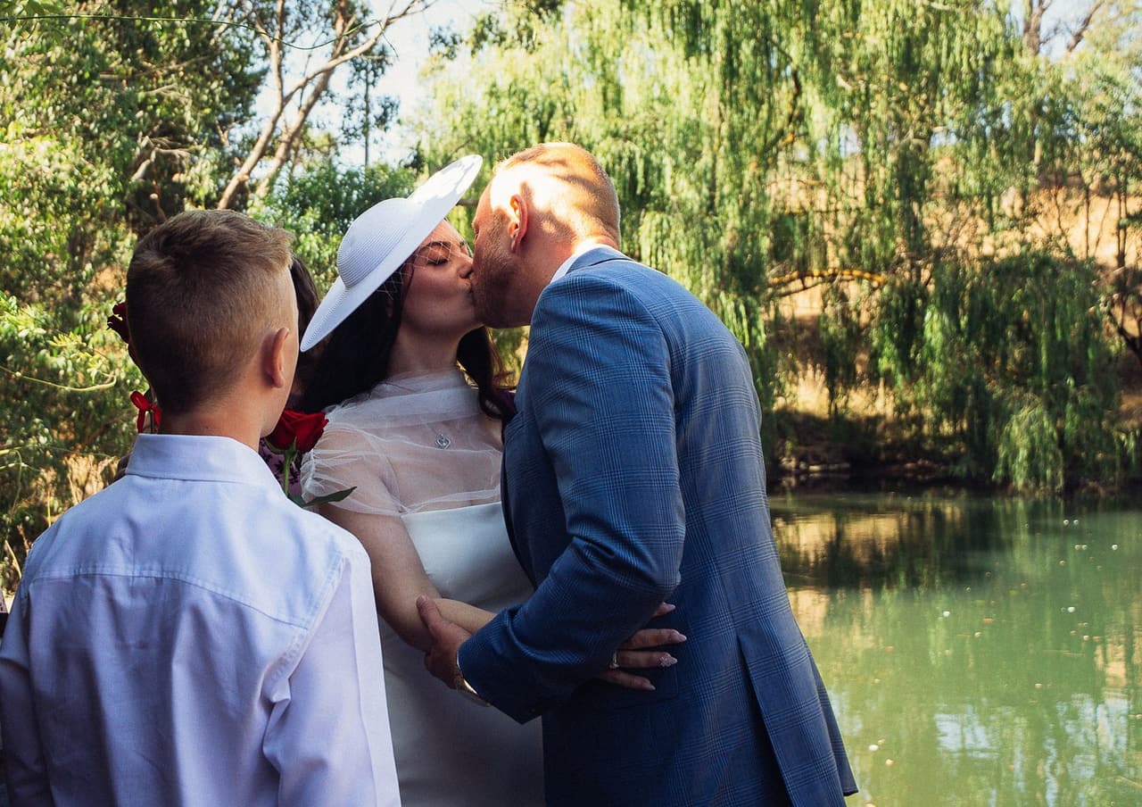 Kim and Ben kissing at the end of their ceremony beside the water