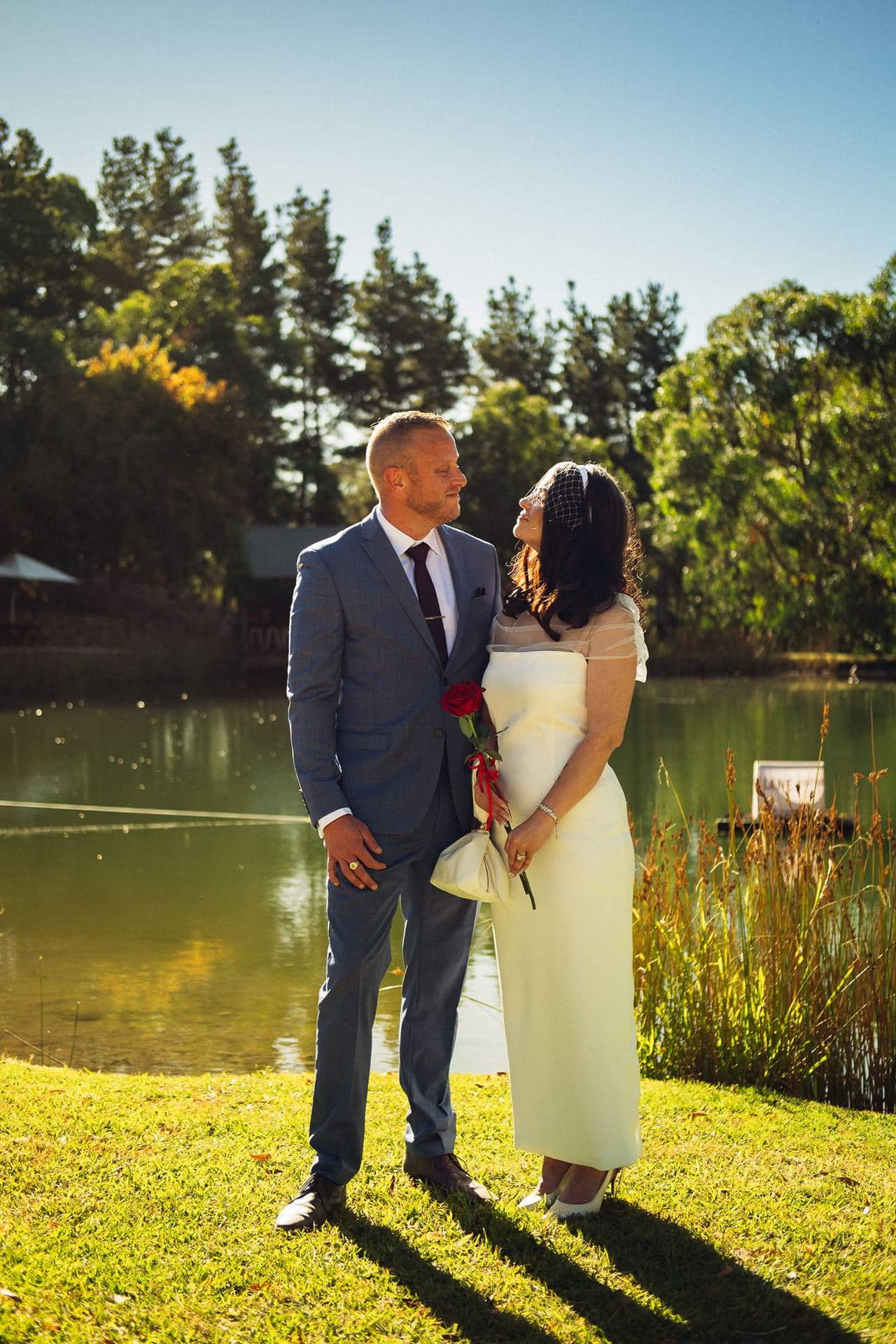 Kim and Ben standing together on the lawn by the pond in the late sun, their long shadows on the grass