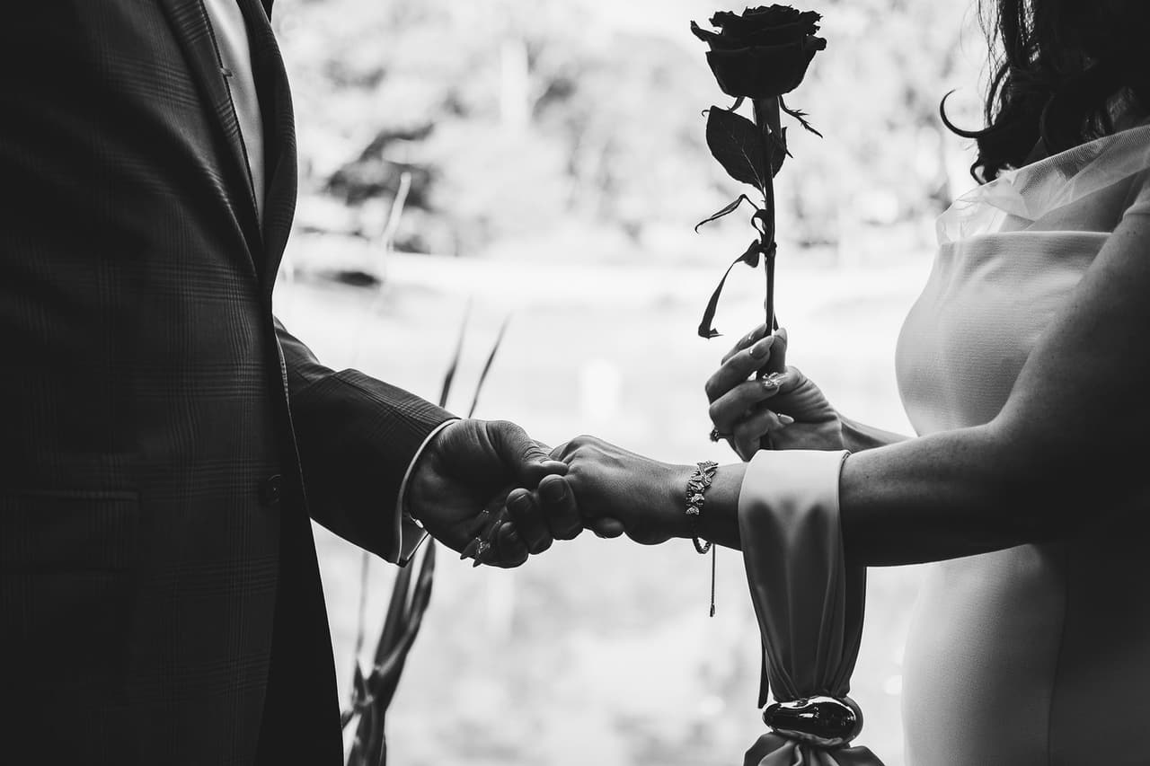 Black and white close up of Kim and Ben’s hands around a single red rose