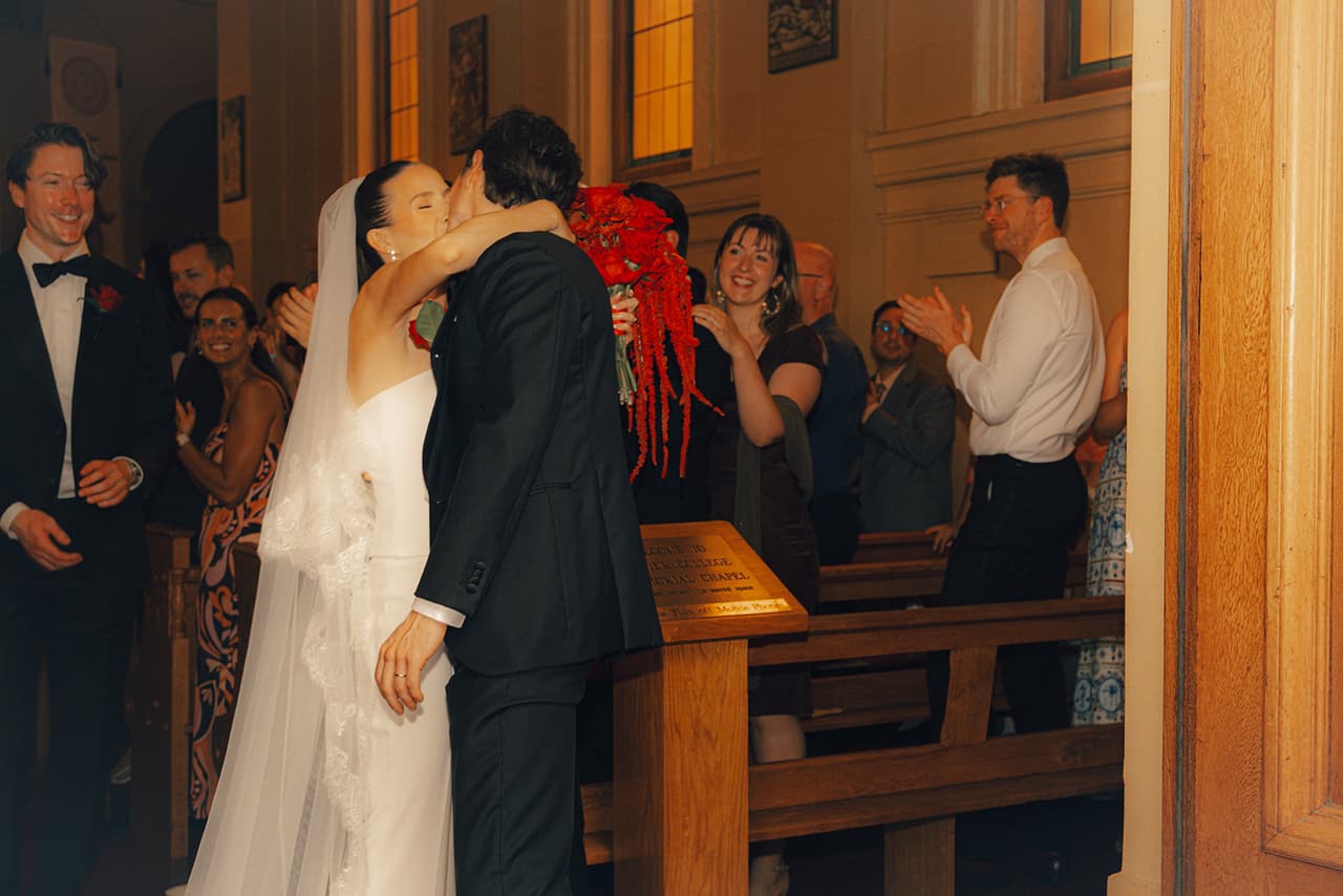 Kira and Nick kissing at the back of the chapel as their guests clap
