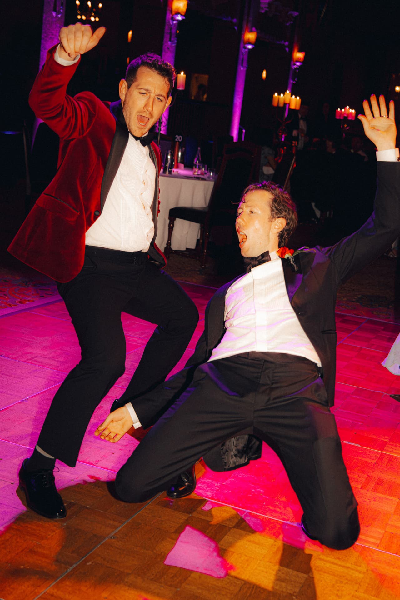 Two guests in dinner suits dancing wildly on a dance floor lit pink and red