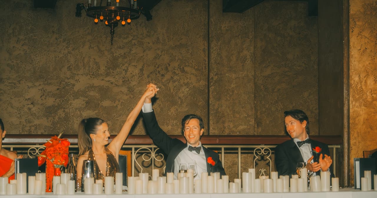 Kira and friends raising their hands at the head table behind a row of candles