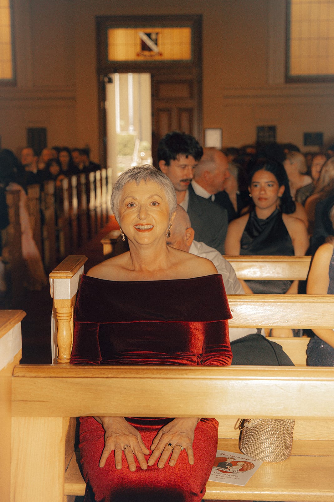 A guest in burgundy velvet smiling from the pews before the ceremony