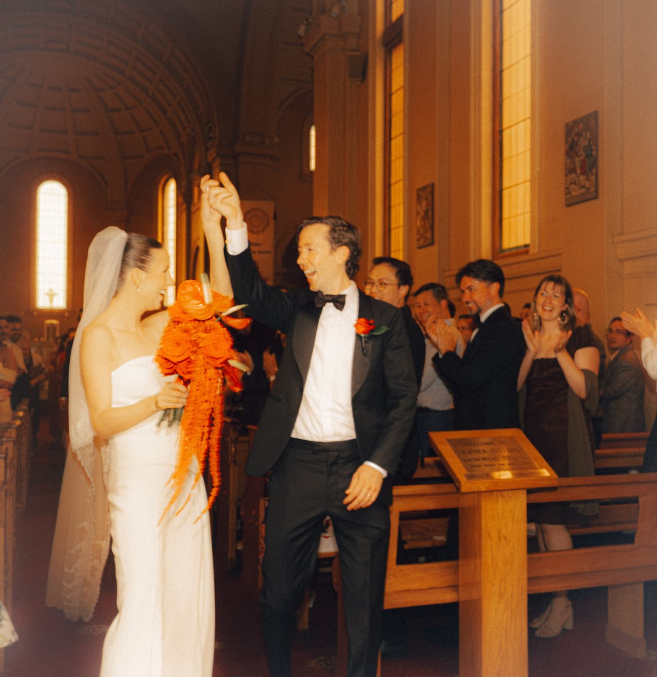 Nick raising his fist as he and Kira walk back down the aisle while guests clap