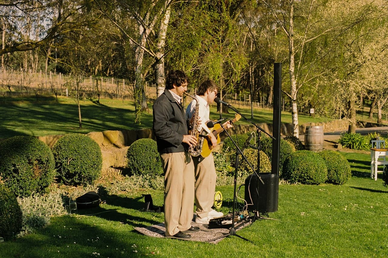 A saxophonist and a guitarist playing on a rug among the clipped hedges before the ceremony, on 35mm film