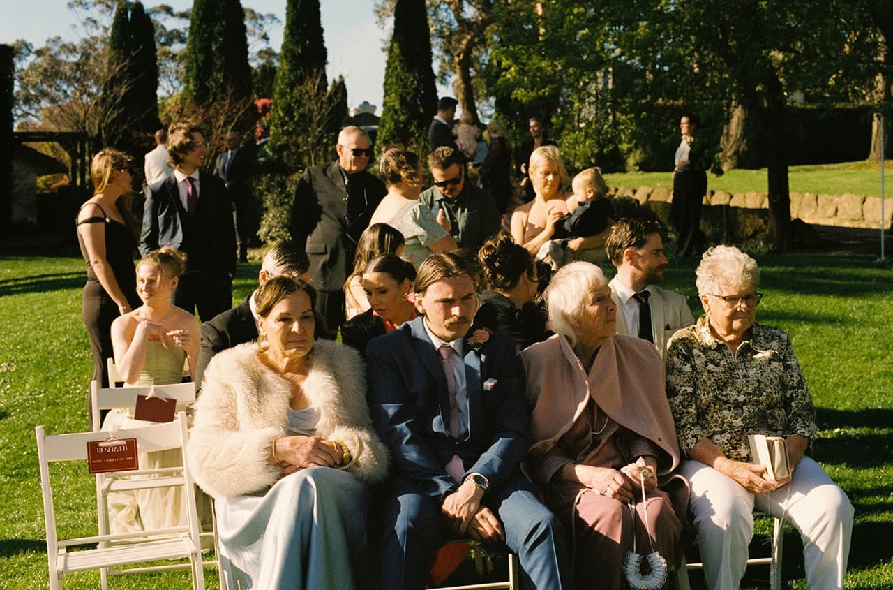 Family in the front row of white folding chairs waiting for the ceremony to begin, on 35mm film