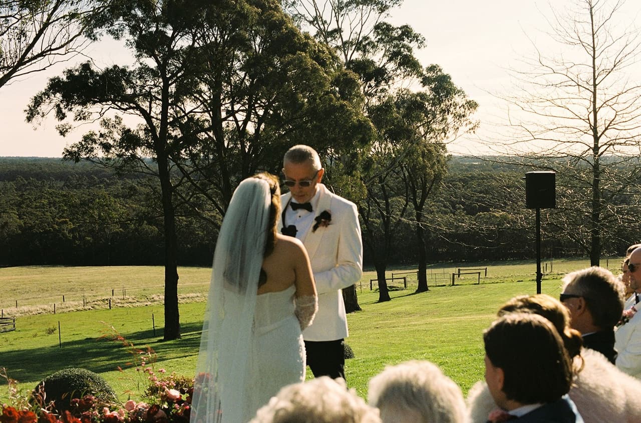 Kristie facing Gareth during the ceremony, the paddocks and the valley stretching out behind them, on 35mm film