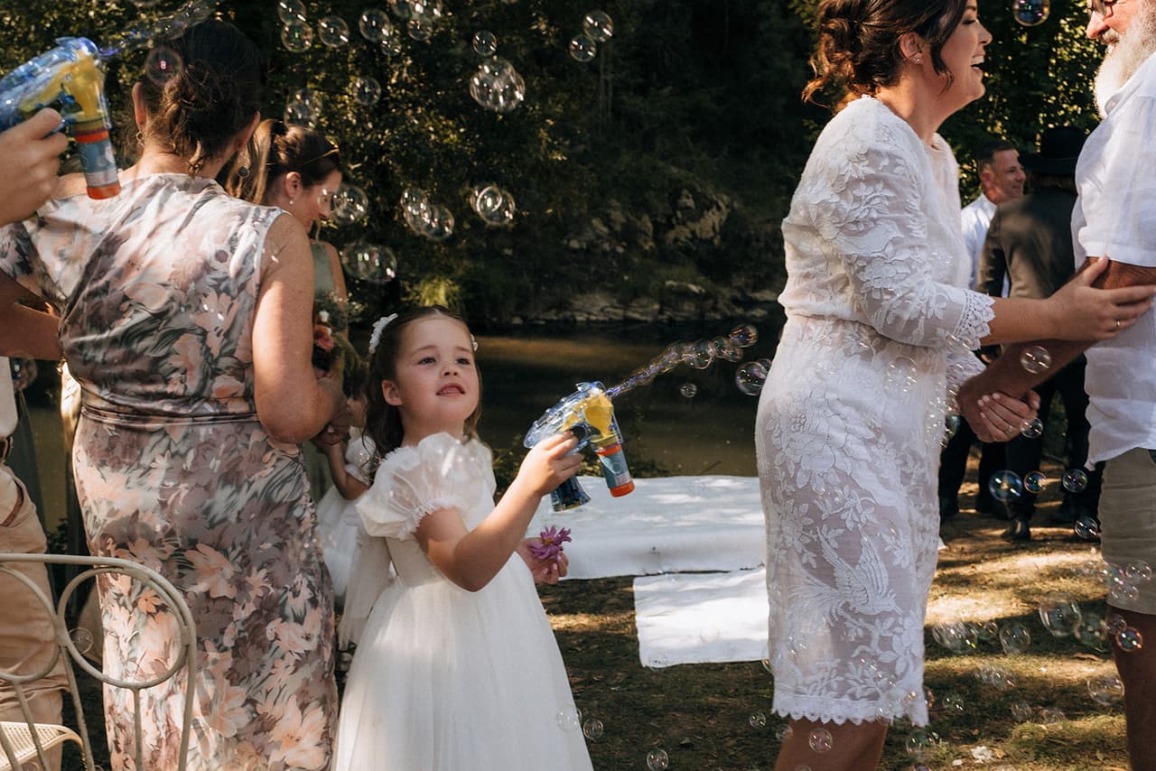 A flower girl firing a bubble gun at Lana as the guests celebrate after the ceremony