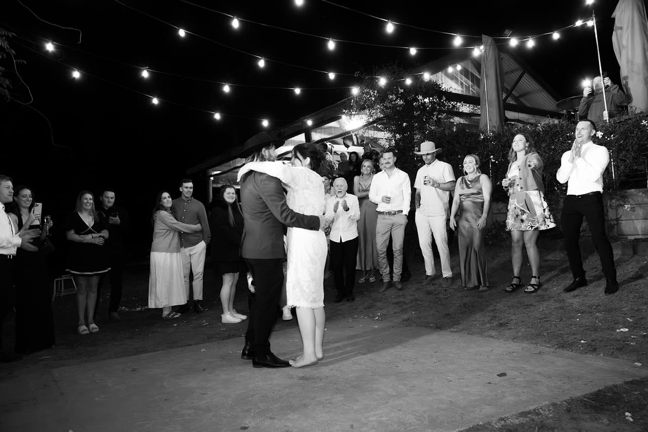 Black and white photo of Lana and Todd’s first dance under the festoon lights, their guests in a circle around them