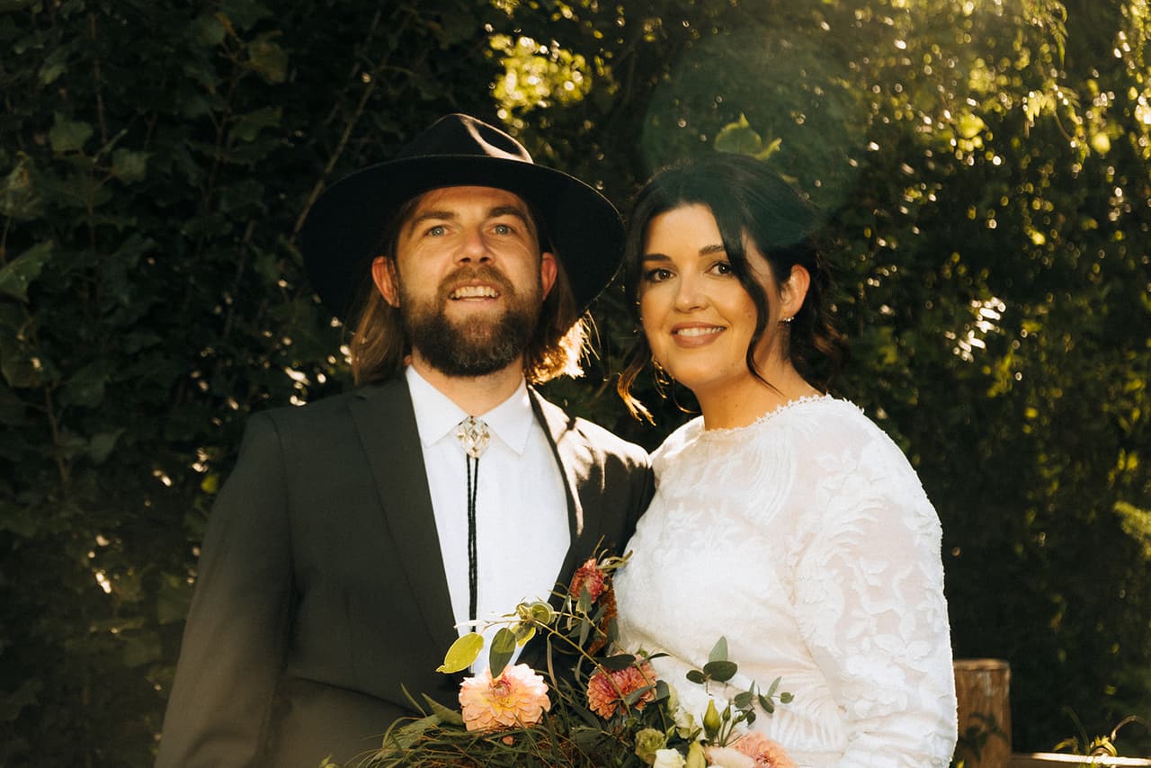 Lana and Todd close together in the trees, her bouquet of dried flowers between them