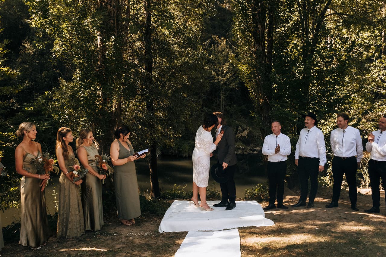 Lana and Todd’s first kiss on the white rug in the grove, bridesmaids on one side and groomsmen on the other