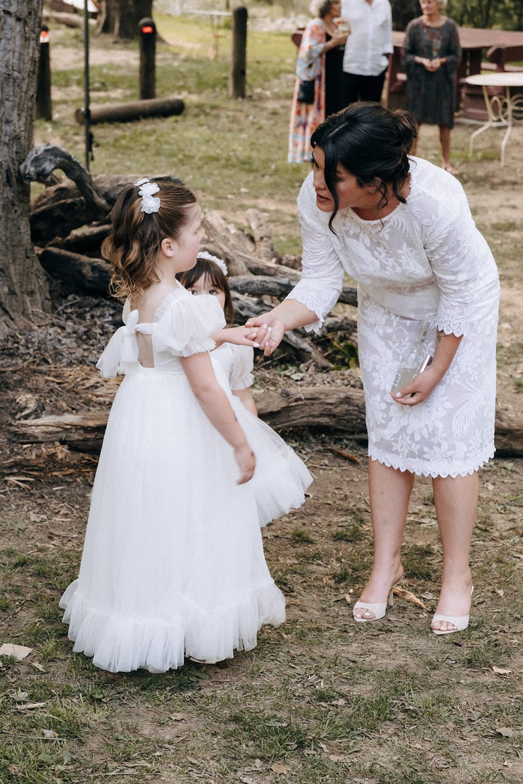 Lana bending down to a flower girl on the lawn under the trees
