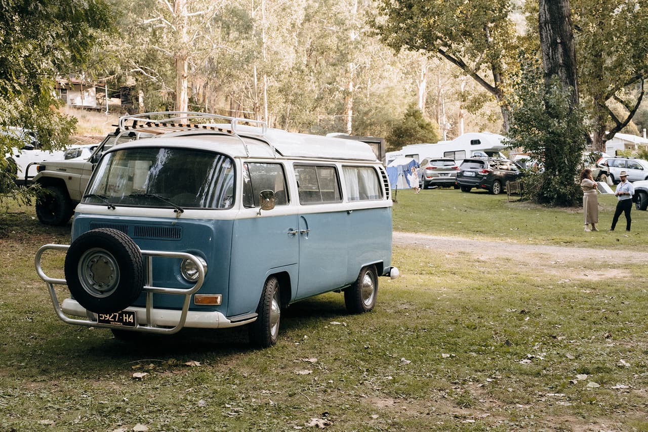 A pale blue Kombi van parked on the grass among the campers