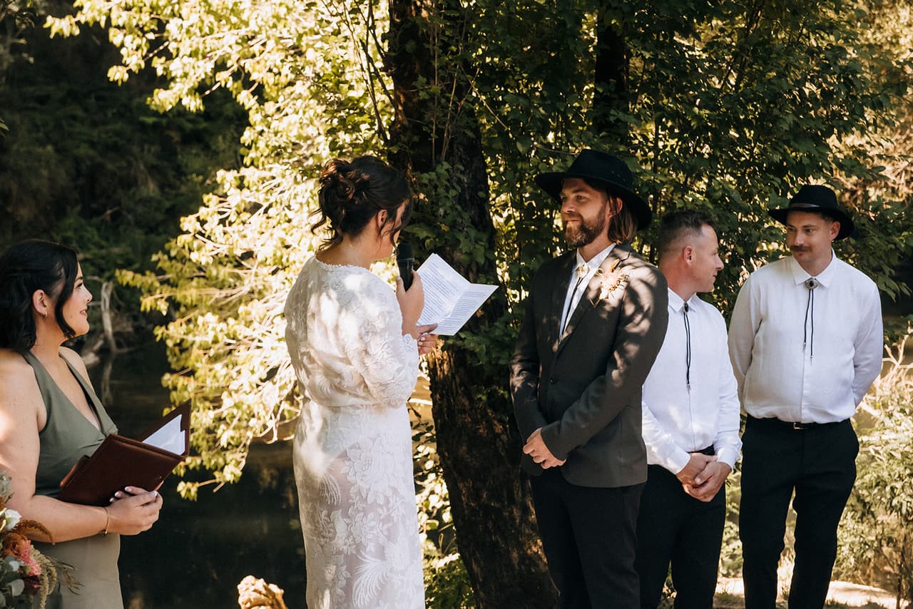 Lana reading her vows into the microphone while Todd smiles at her