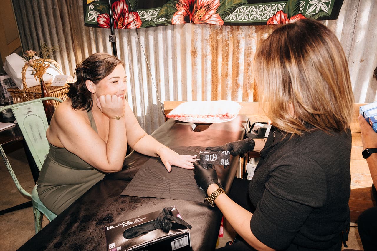 A bridesmaid laughing as she gets a tattoo at the reception