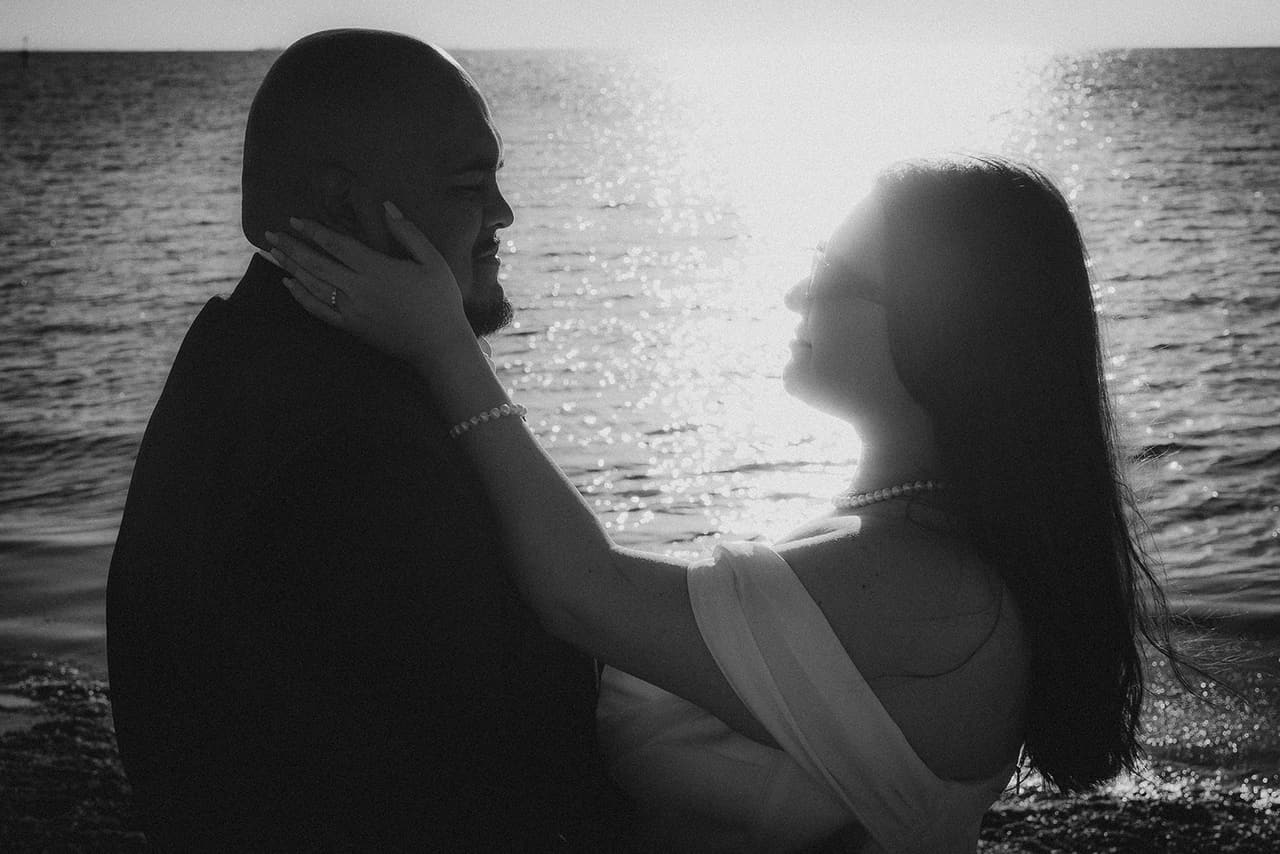 Black and white photo of Martina resting her hand on Diego’s cheek, the sea shining behind them