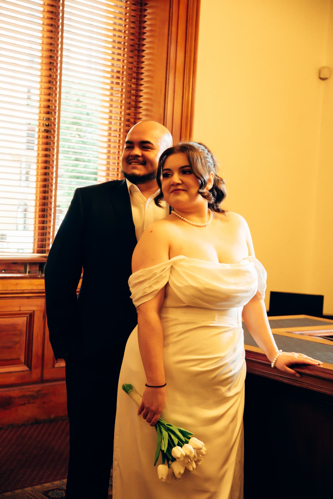 Martina leaning on the registry desk with Diego close behind her by the tall window