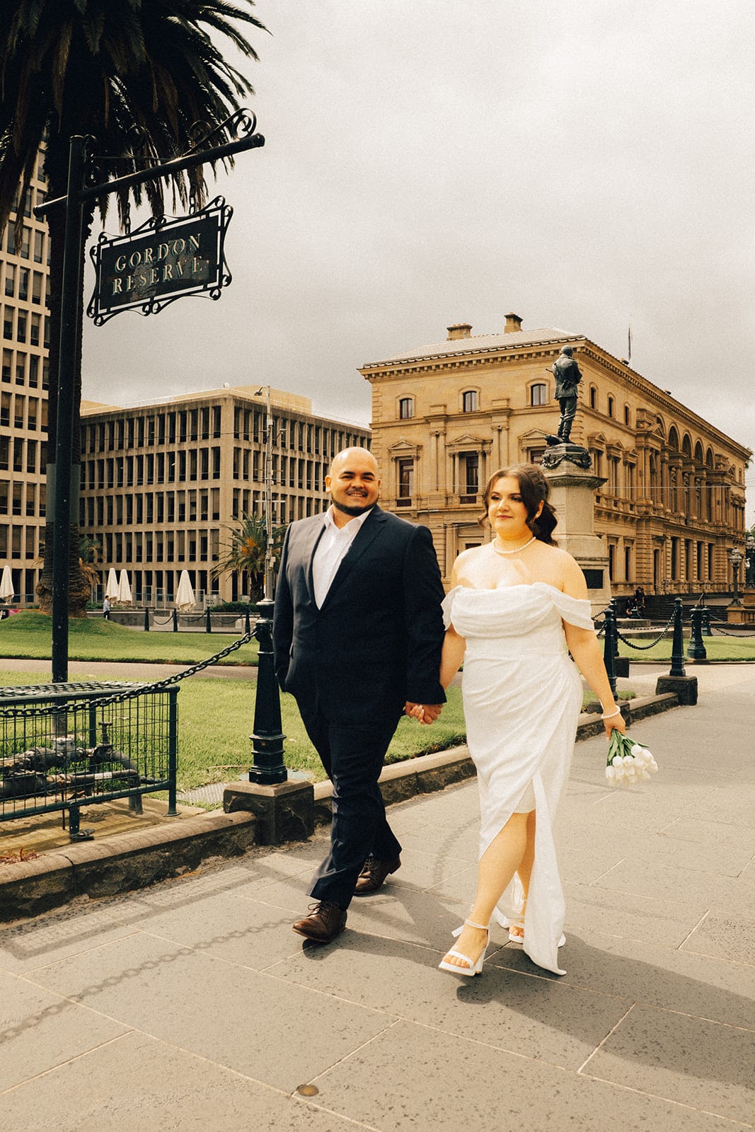 Martina and Diego walking along the footpath past the Gordon Reserve sign, sandstone buildings behind them