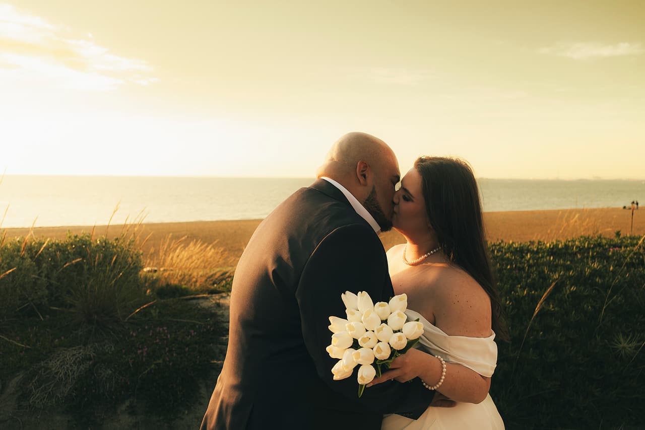 Martina and Diego kissing among the grasses above the beach as the sun goes down
