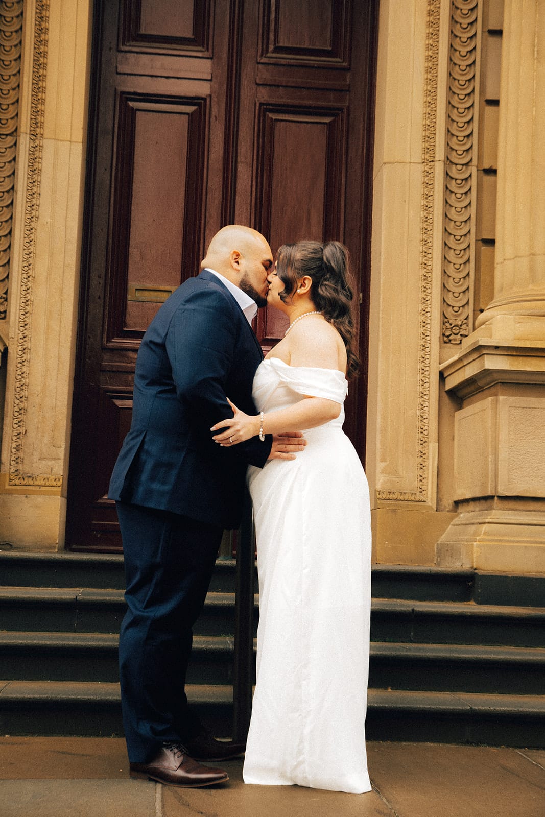 Martina and Diego kissing on the steps in front of the tall red timber door