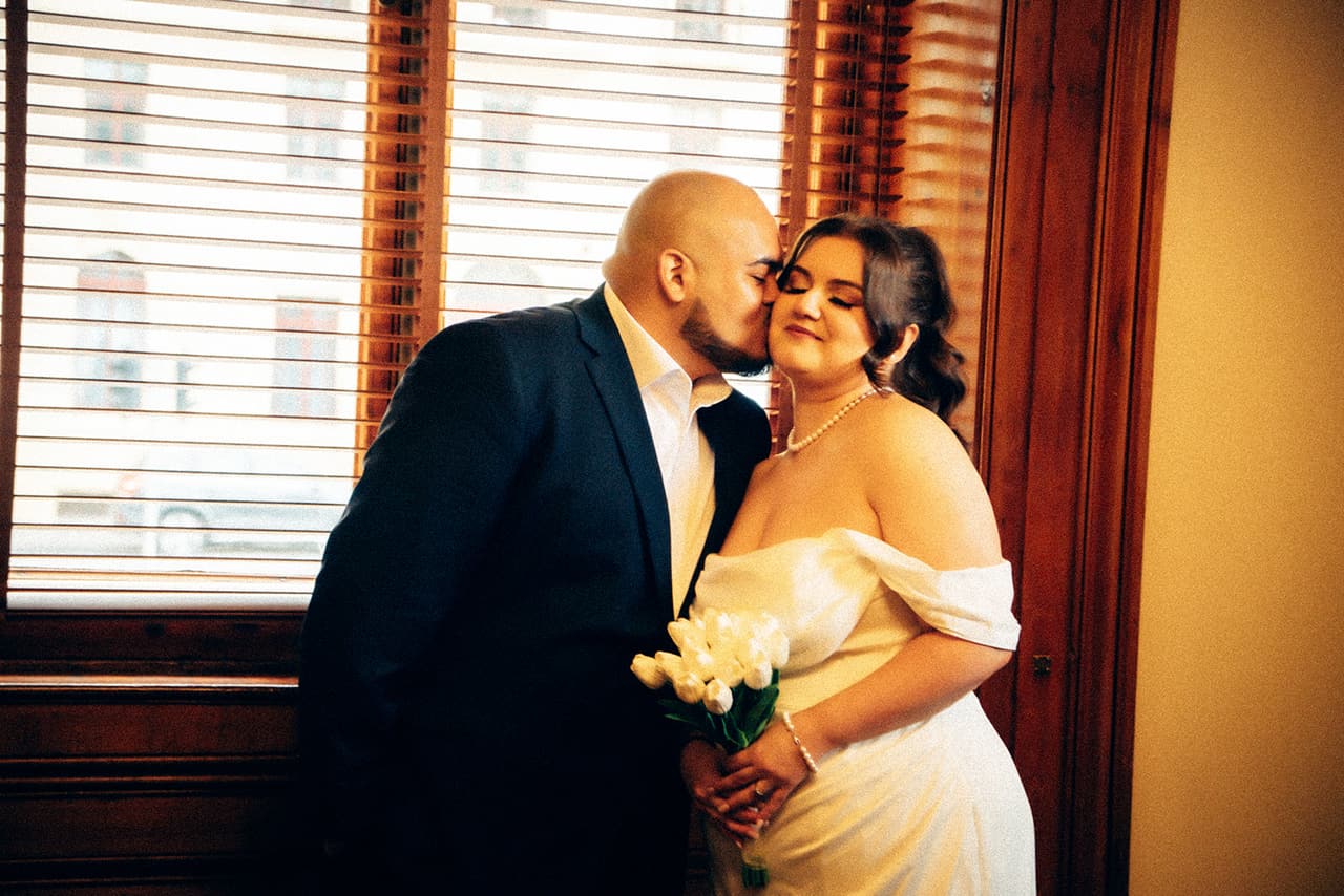 Diego kissing Martina's cheek by the registry's tall windows