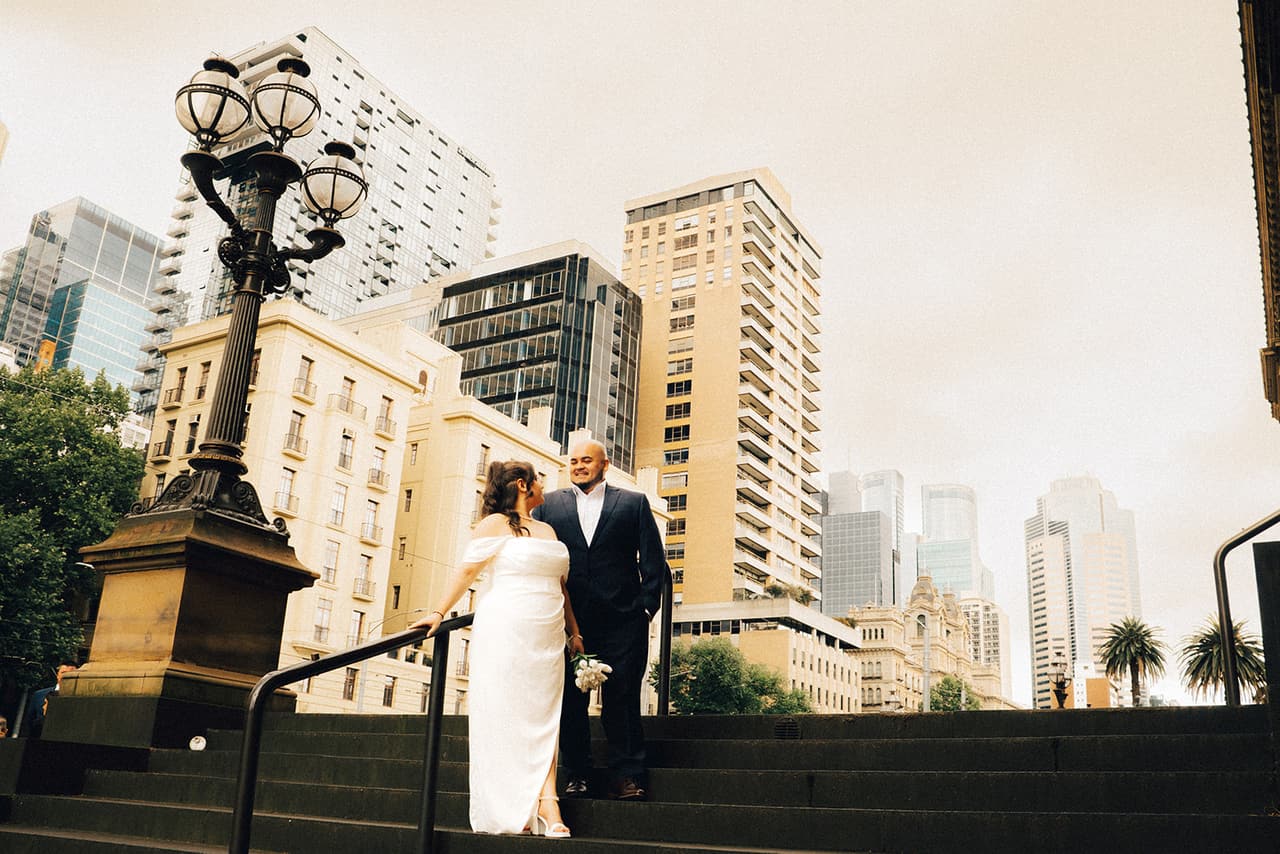 Martina and Diego on the steps beside the old lamps, the city's towers rising behind them