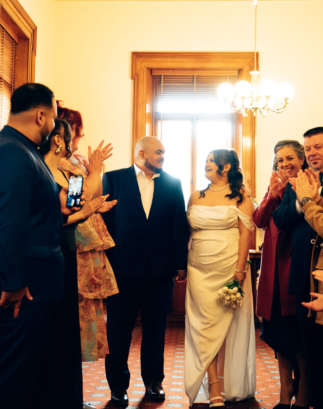 Guests clapping and holding up a phone as Martina and Diego walk out of the ceremony room