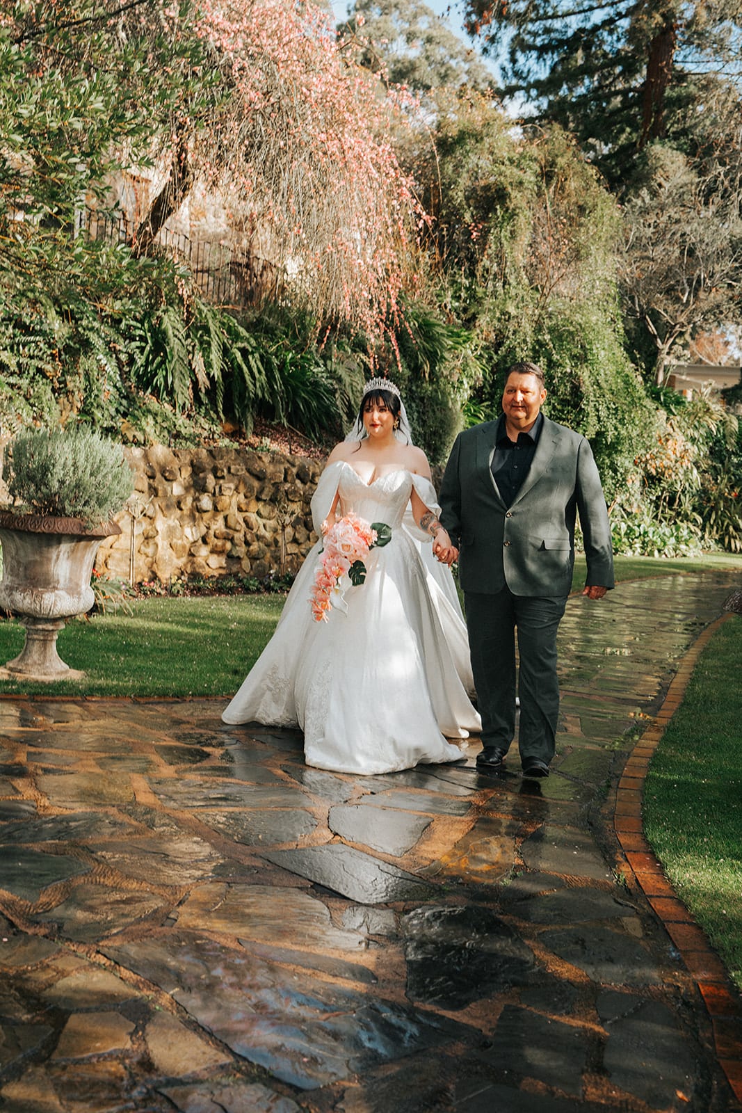 Porscha walking to the ceremony on her dad's arm along the wet stone path, her veil trailing behind