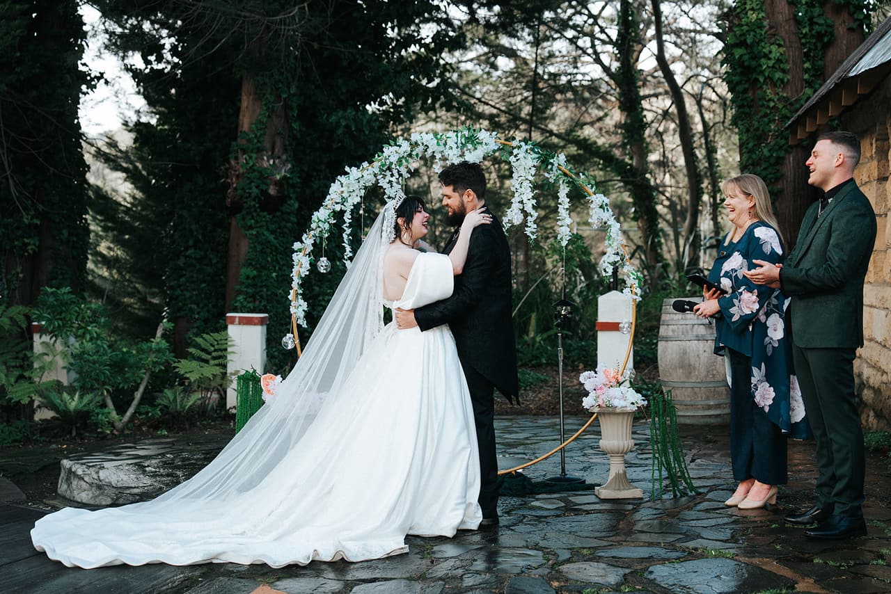 Porscha and Jordan kissing under the floral arch, her long train spread over the stone