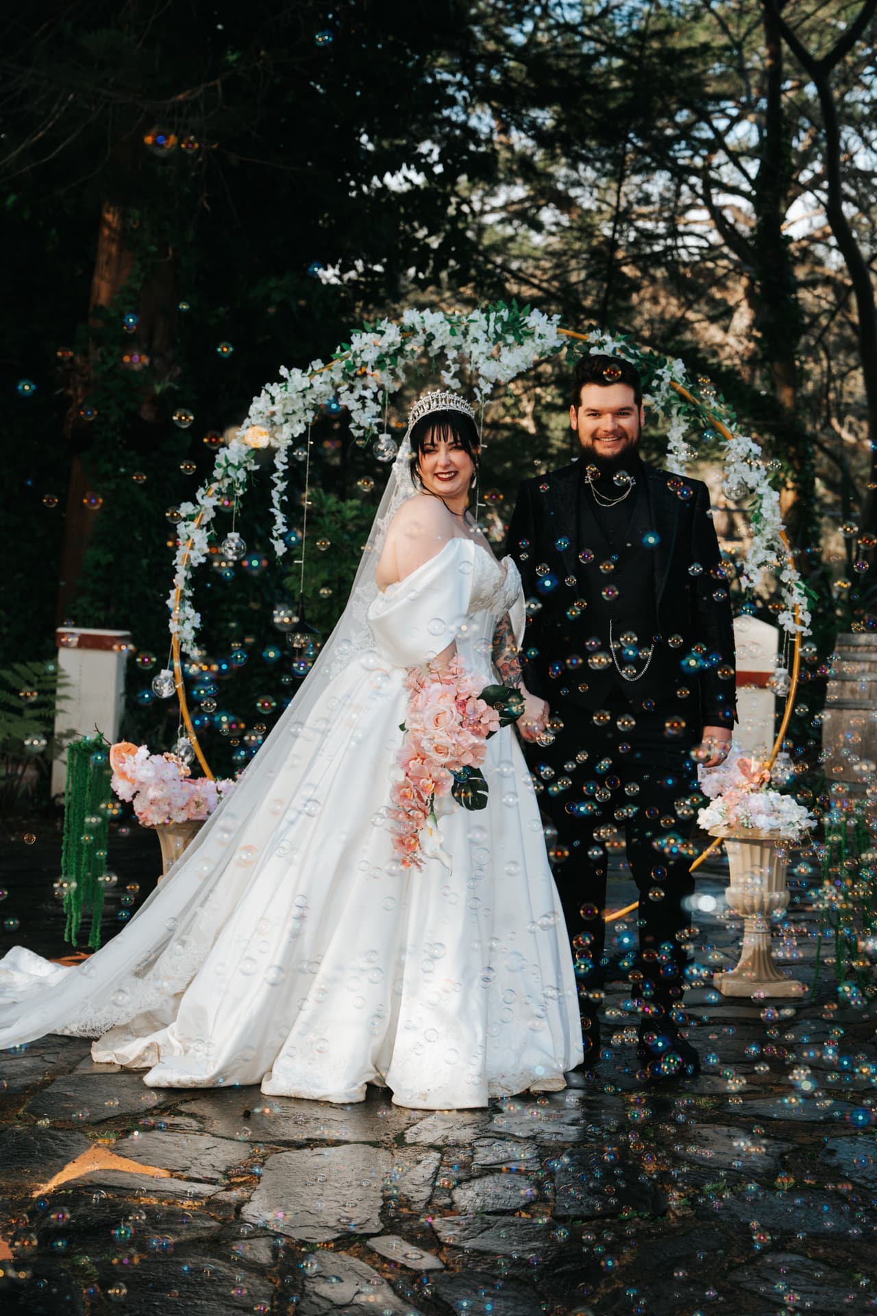 Porscha and Jordan walking out through a shower of bubbles beneath a floral arch