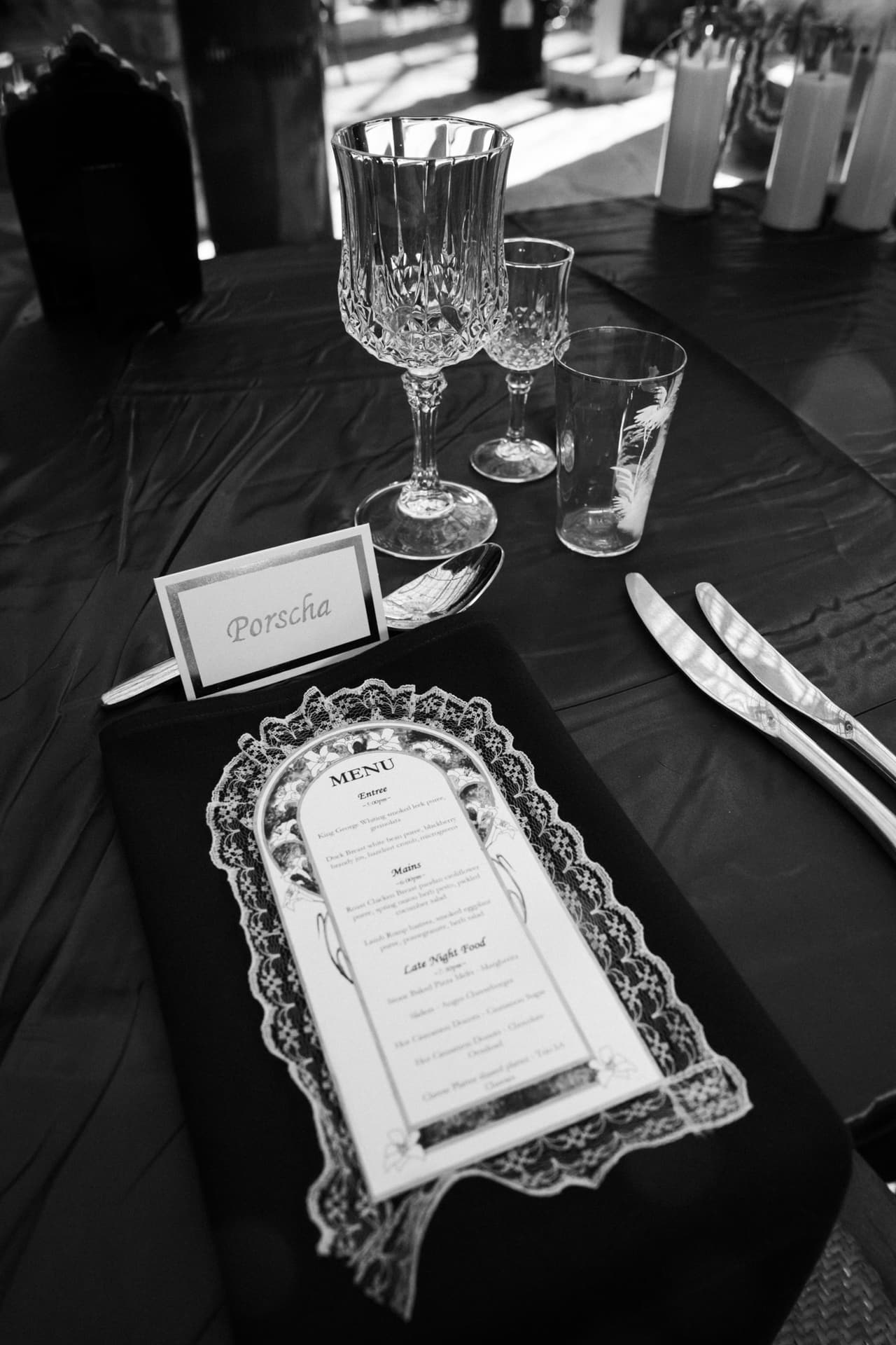 Black and white photo of a place card for Porscha beside crystal glasses and a lace-framed menu