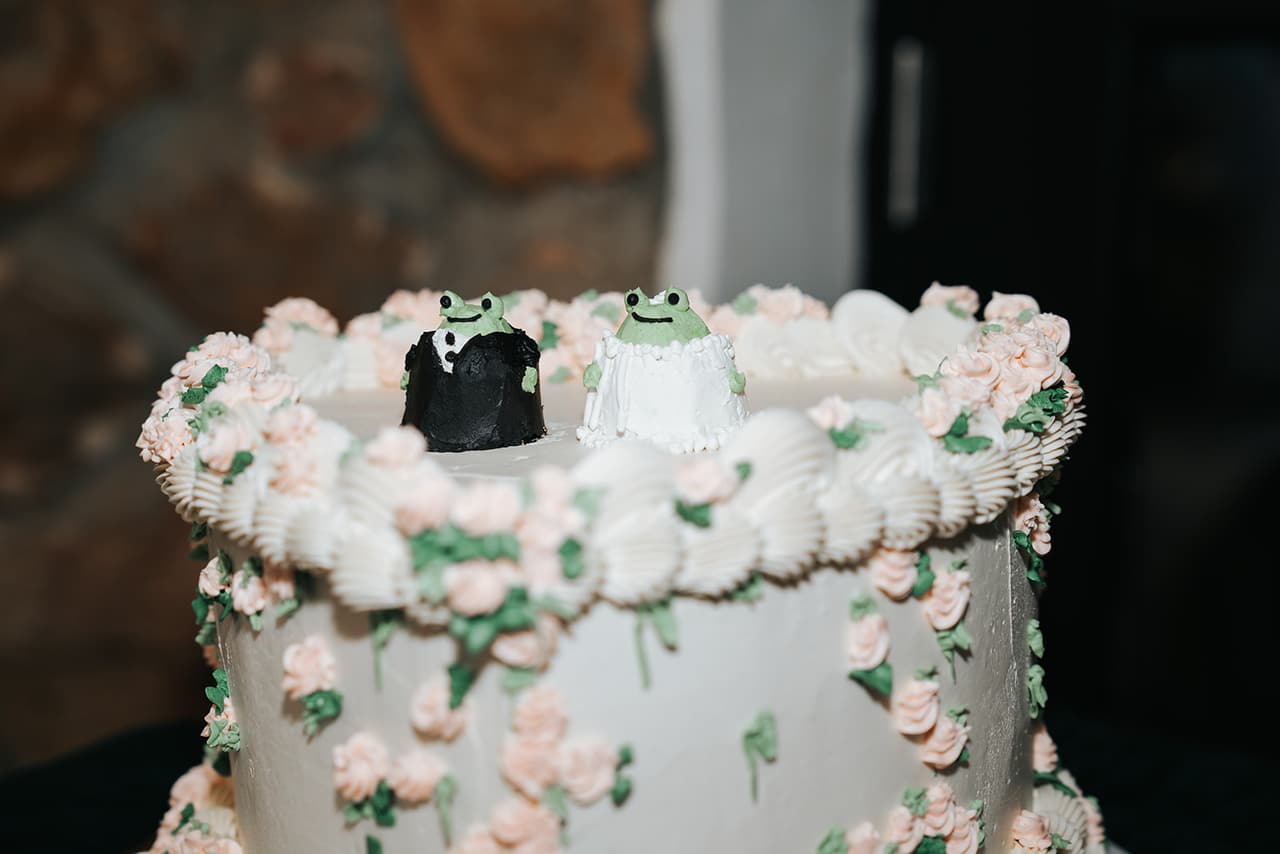 Close up of the white wedding cake with pink sugar flowers and a black heart on top