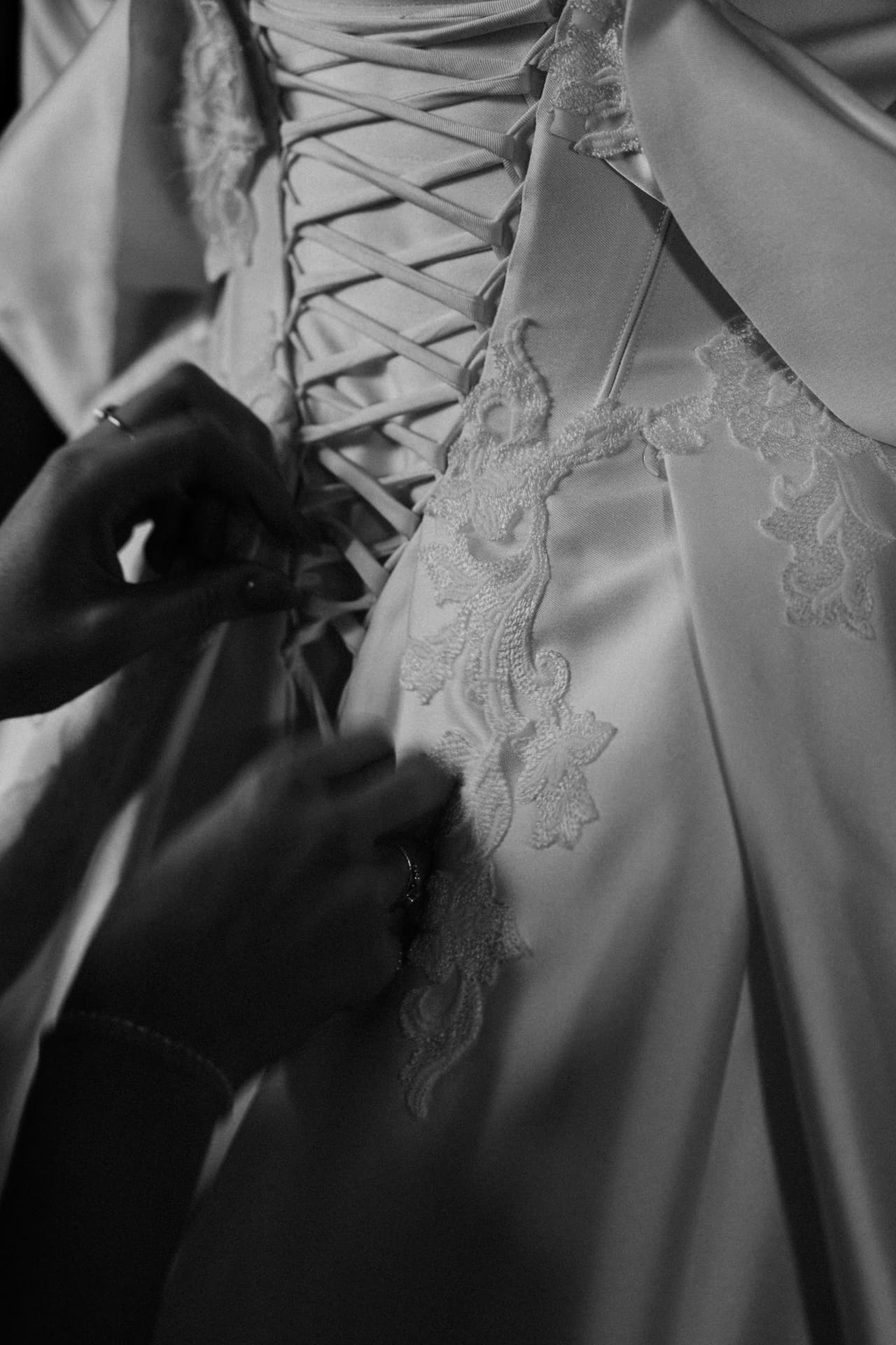 Black and white close up of hands lacing up the back of Porscha’s gown