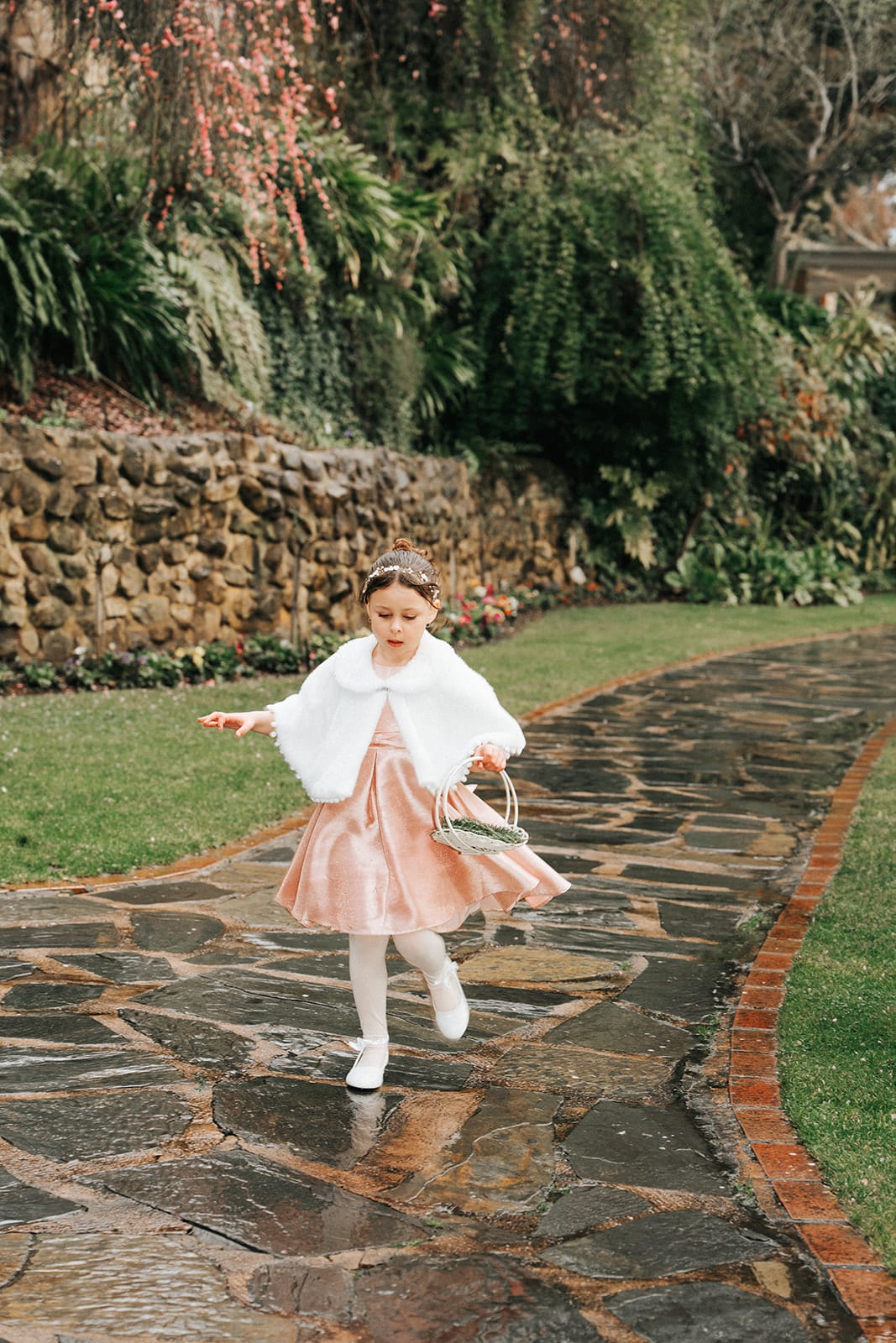 The flower girl in a pink coat running down the wet stone path