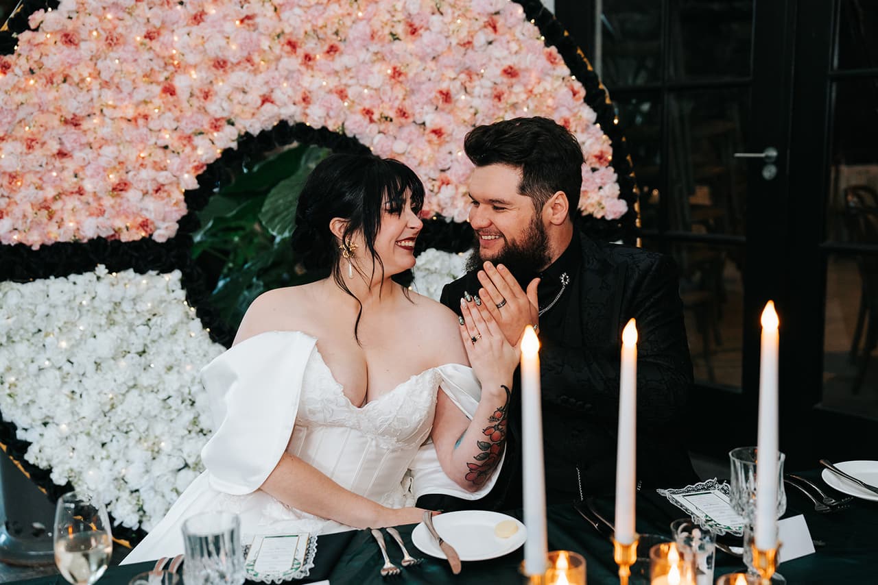 Porscha and Jordan laughing at the head table in front of the Poké Ball flower wall