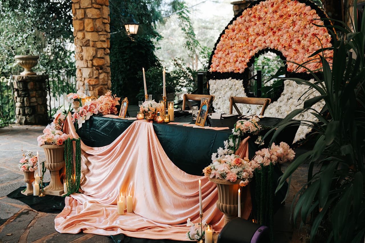 The head table in front of a giant Poké Ball made of pink and white flowers, green and peach silk below