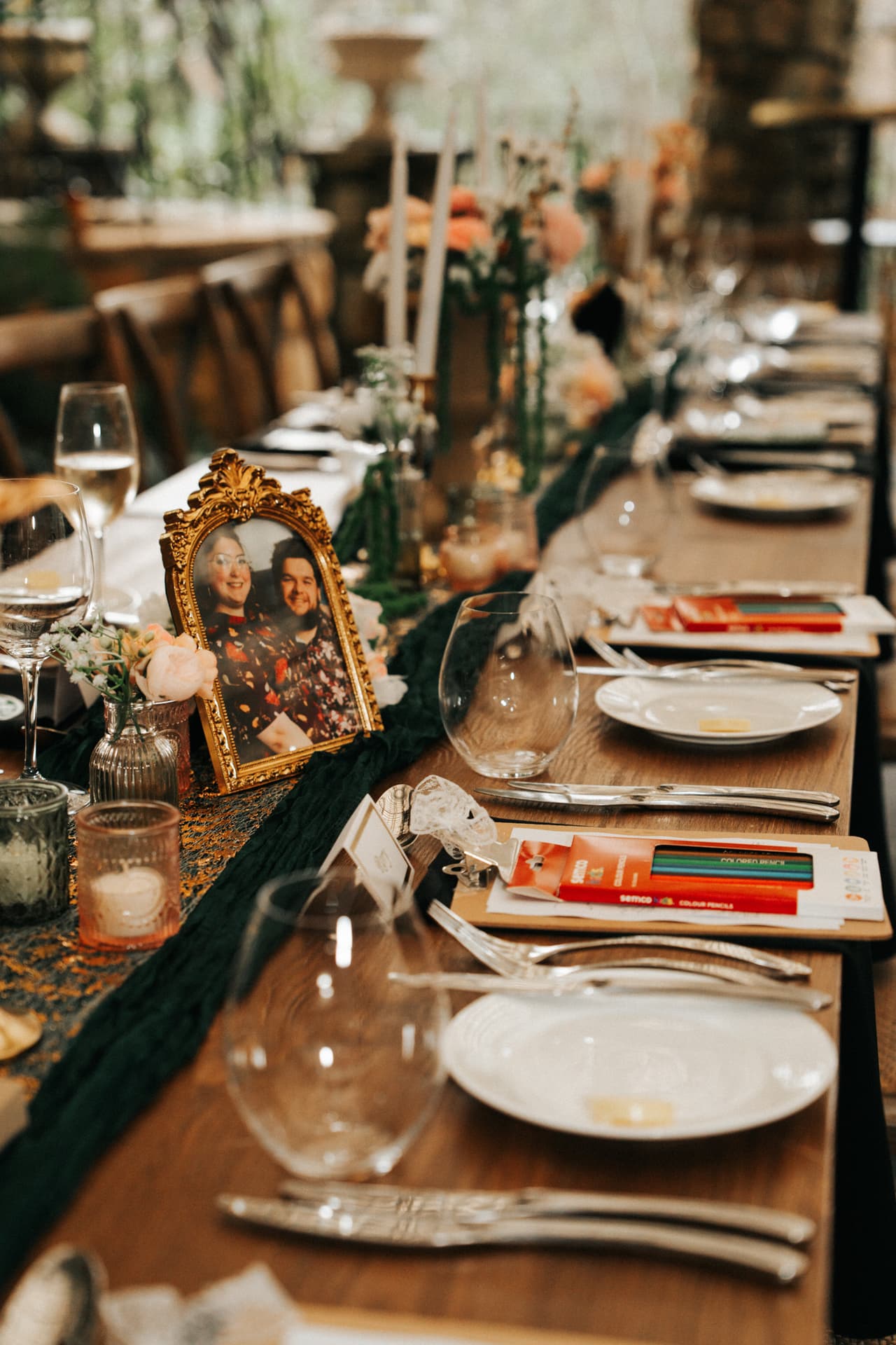 Long reception tables set with candles, green runners and a gold-framed photo of the couple