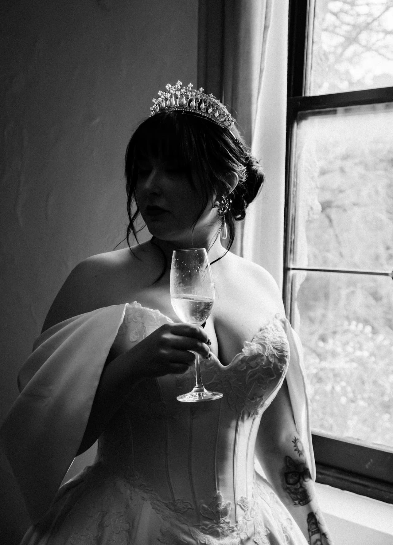 Black and white photo of Porscha in a tiara holding a glass of champagne by a window