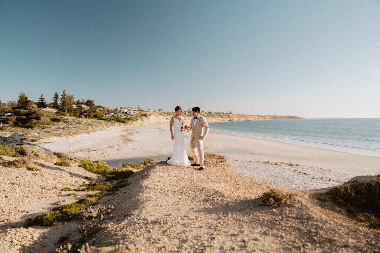Sayuri and Shuto standing on a sandy point above the long curve of the beach in afternoon sun