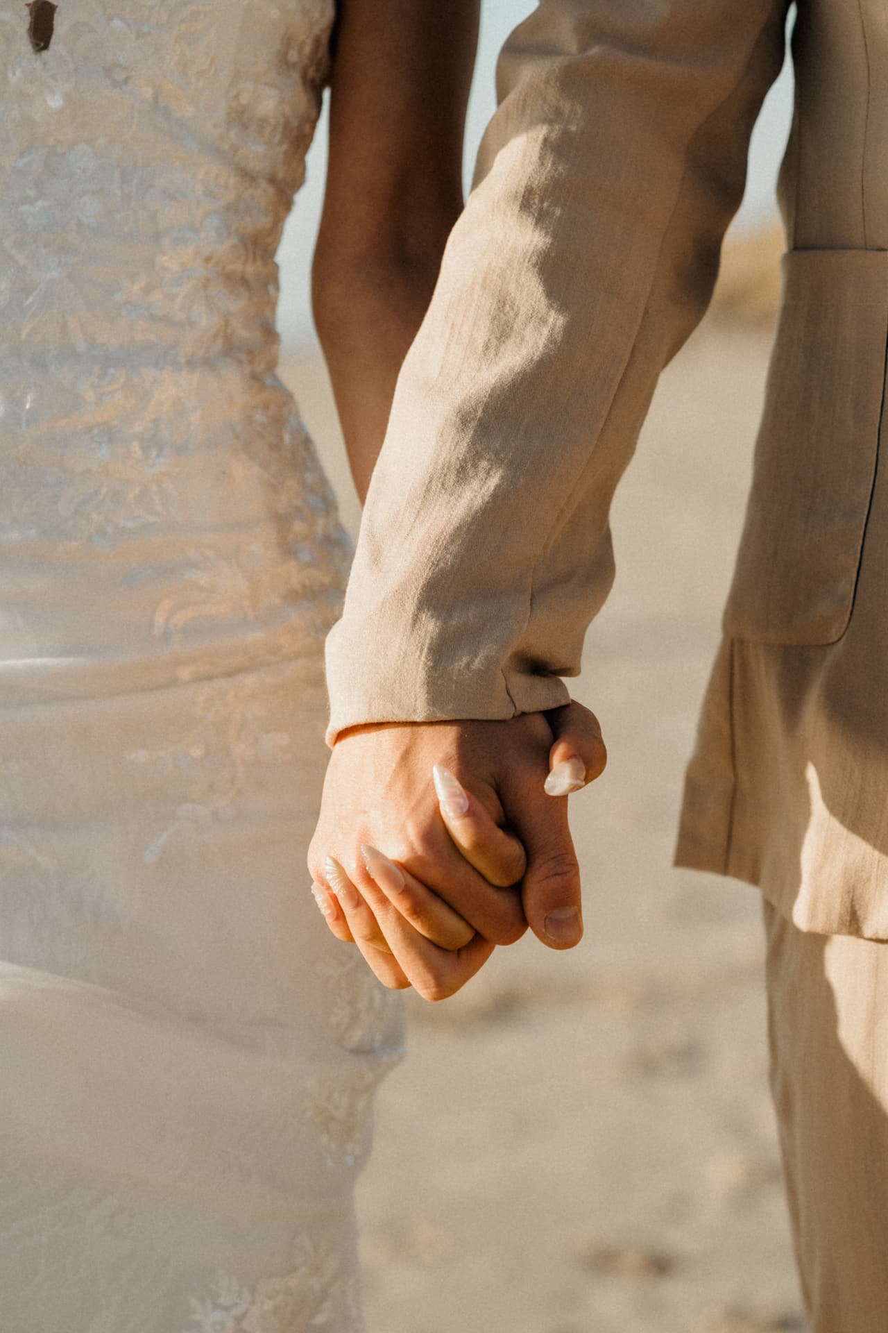 Close up of Sayuri and Shuto holding hands, her lace gown beside his beige suit