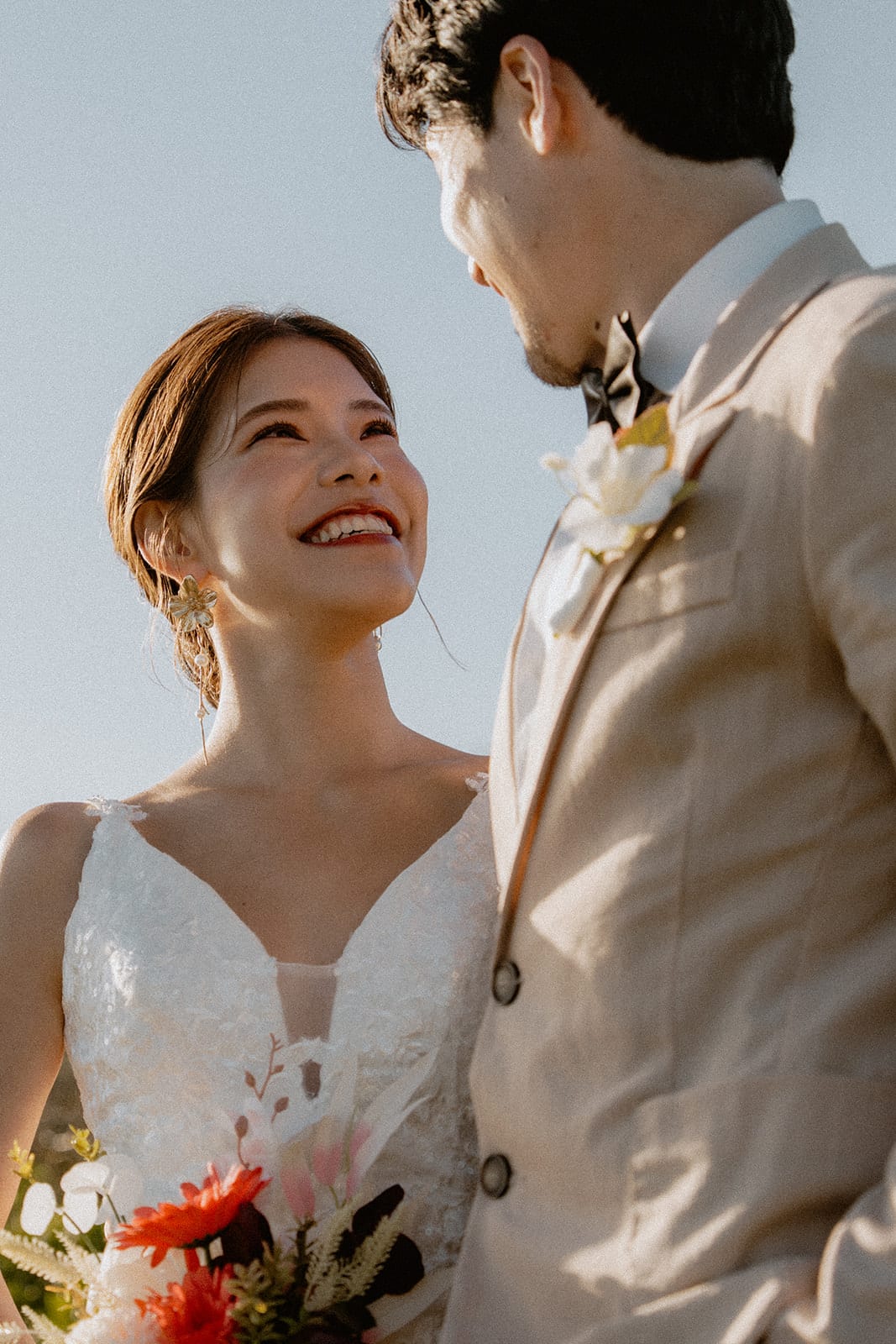 Sayuri laughing up at Shuto on the clifftop, her bouquet of red and orange flowers in hand