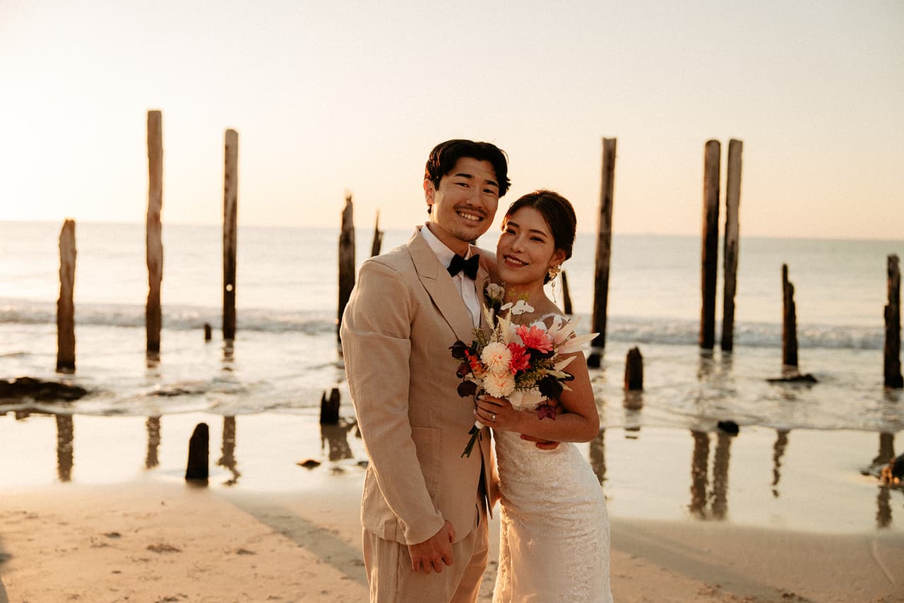 Shuto and Sayuri laughing towards the camera among the old jetty posts in the low sun