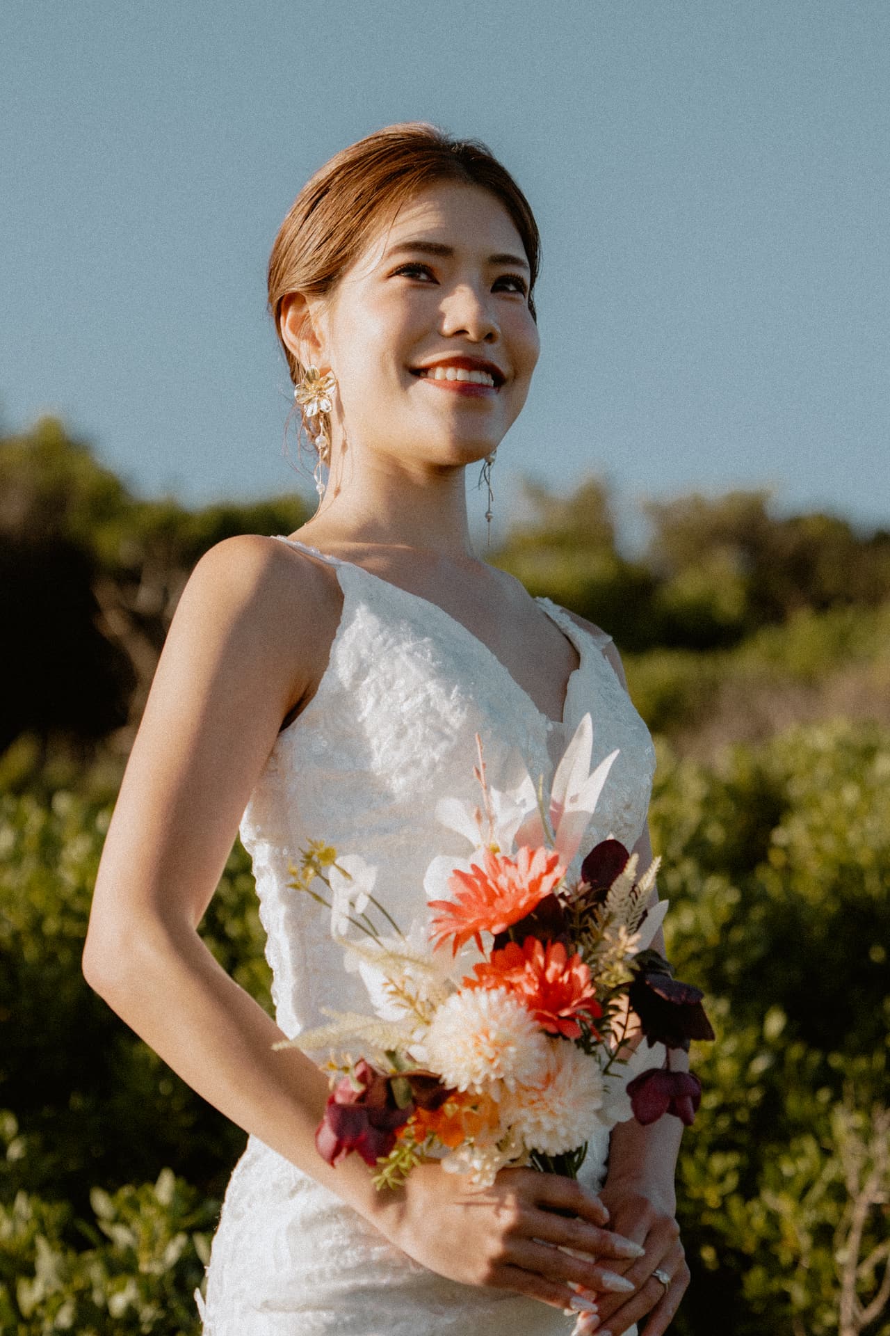 Sayuri smiling with her bouquet among the coastal bushes on the clifftop